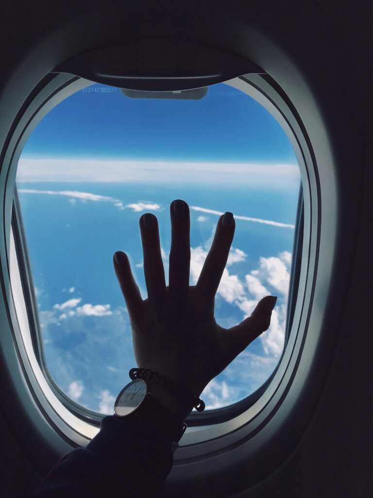 Silhouette of a hand touching an airplane window with a view of clouds and the sky.
