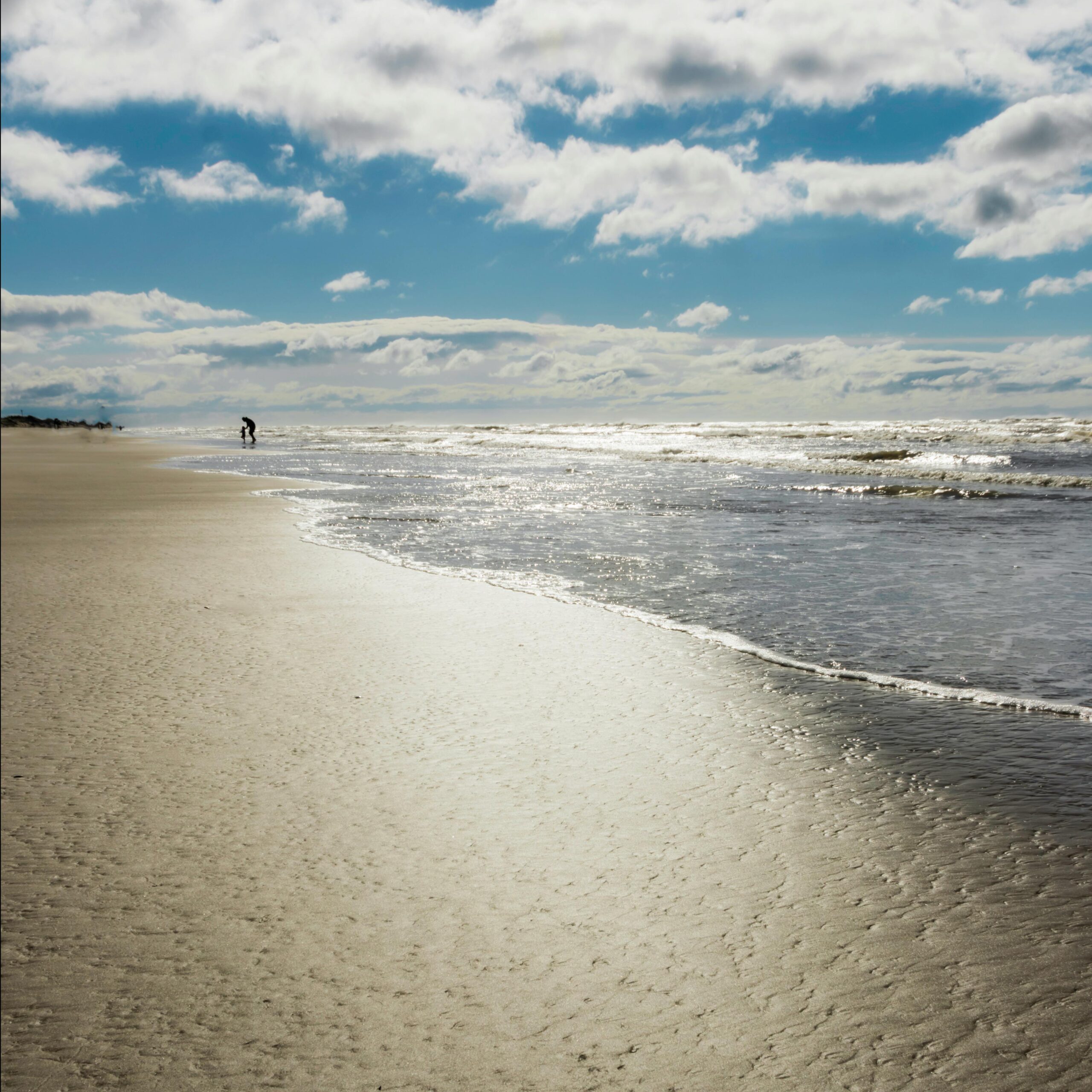 Tranquil sunny day at Tramandaí Beach with shimmering sand and cloudy sky.